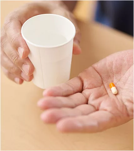 Hands holding a paper cup and a yellow pill 