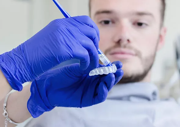 close up of teeth whitening tray being prepared with patient in the background